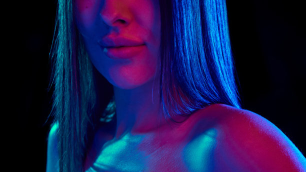 特写照片展示女性丰满、滋润的嘴唇，在黑色摄影棚背景下闪耀着明亮的霓虹蓝粉色光芒。图片下载