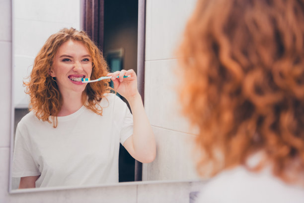 年轻女性在早晨室内浴室里用牙刷刷牙并照镜子的照片图片下载