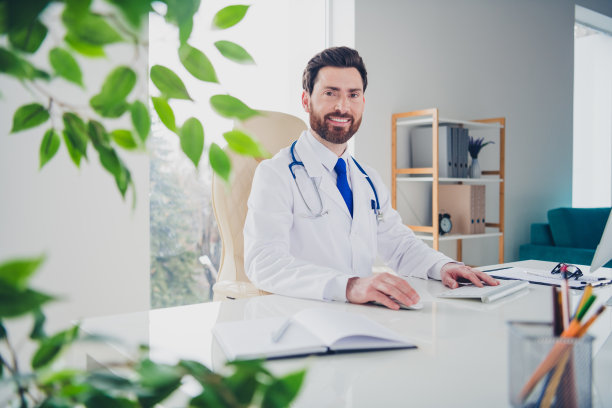 合格的男医生坐在白色医院办公室的桌子前进行在线咨询的照片图片下载
