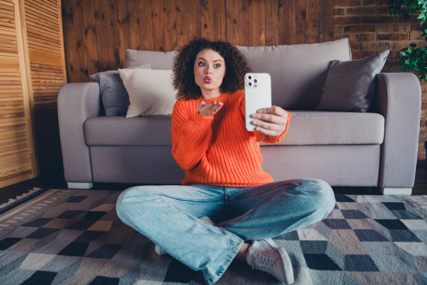 漂亮年轻女性在公寓室内用智能手机自拍并送出空气吻的全身照片图片下载