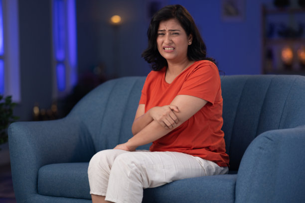 女人坐在家里的沙发上，肘部疼痛的库存照片图片下载