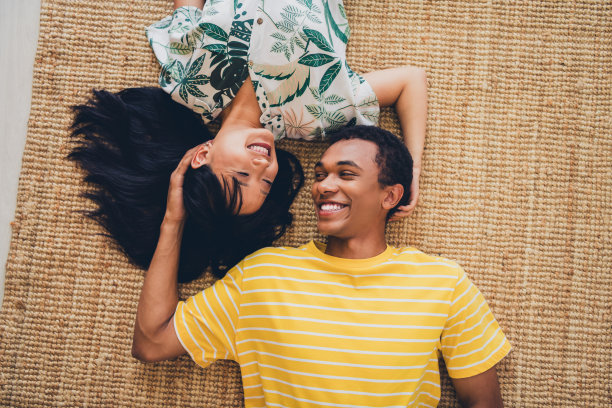 高角度视图照片，展示了一对可爱甜美的跨国夫妻穿着T恤躺在室内地板上。图片下载