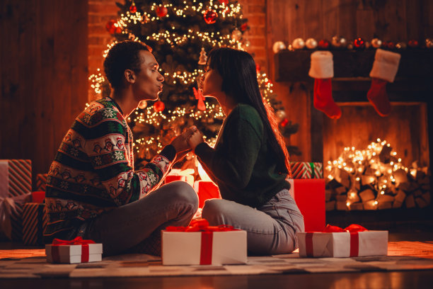 可爱的年轻情侣在家居派对装饰的室内房间里，穿着圣诞服装，手牵手亲吻的全身照片图片下载