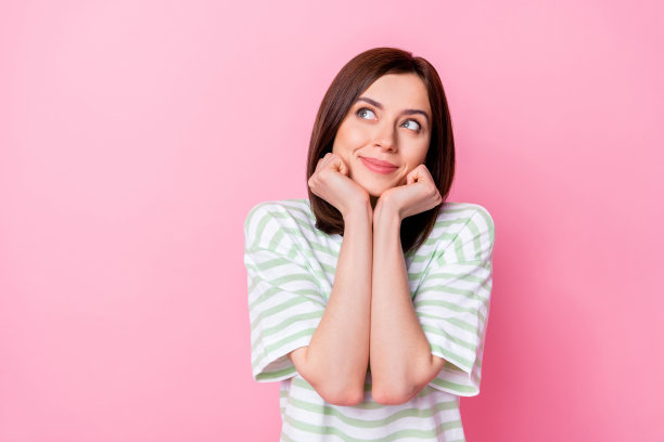 可爱的年轻女士的照片肖像，面带微笑，双手握拳，穿着时尚的条纹衣服，背景为粉色，展现甜美的梦幻气息。图片下载