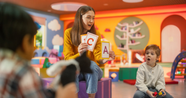 美丽的幼儿园老师与年轻有才华的孩子们一起学习字母。女教师向多元化的儿童群体展示带字母的图片，帮助他们发展知识，学习阅读。图片下载