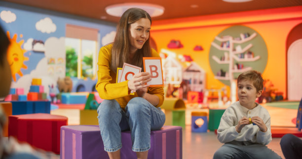 美丽的幼儿园老师与年轻有才华的孩子们一起学习字母。女教师向多元化的儿童群体展示带字母的图片，帮助他们发展知识，学习阅读。图片下载