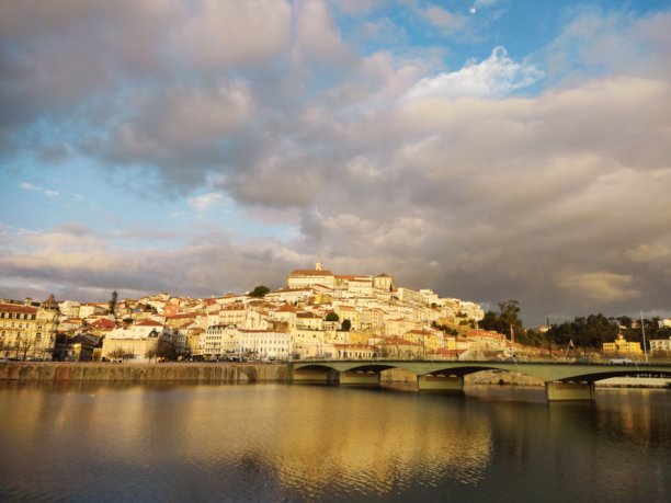 这张图片捕捉了一个建在山坡上的历史城市的美丽景色，可能是葡萄牙的科英布拉，正值黄昏或傍晚的迷人时刻。图片下载
