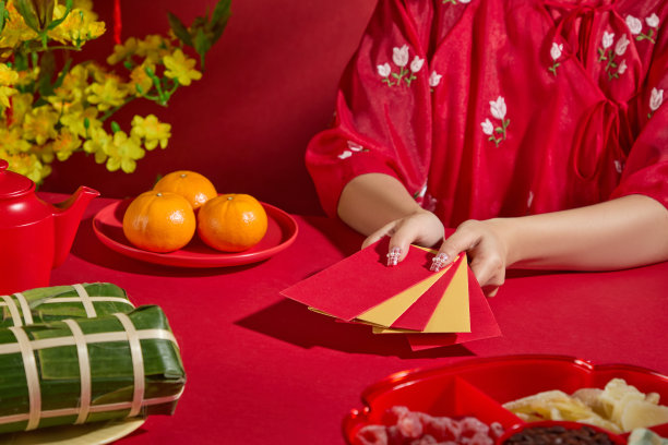 适合新年主题照片，特写一位穿着传统服装的女性模特正在展开一个幸运红包，红色托盘上摆放着春节装饰品。图片下载