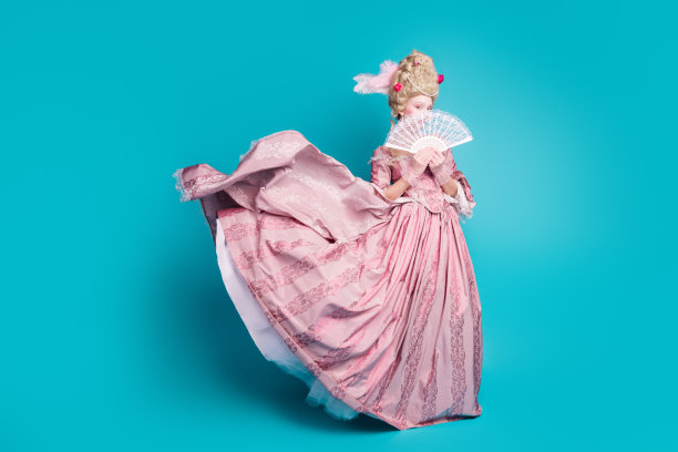 迷人的巴洛克女王穿着紧身胸衣舞会礼服，手持扇子，独立于蓝色背景前的皇家狂欢节照片图片下载