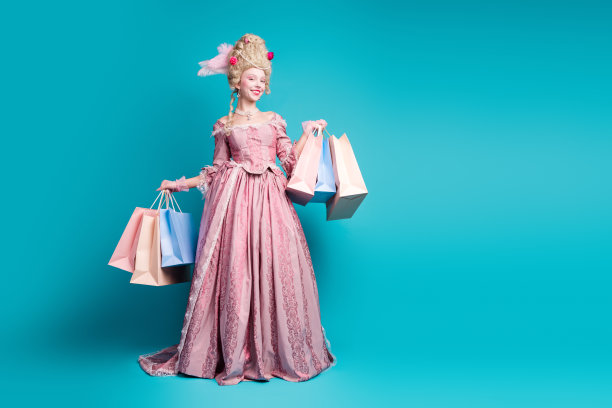 年轻女性穿着文艺复兴女王服装，手持购物袋，背景为青色，空旷的空间中的全身照片图片下载