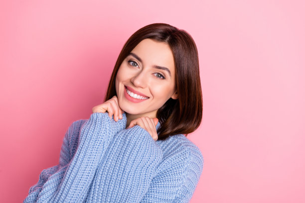 特写照片，年轻可爱的女孩穿着针织毛衣，微笑着展现出可爱的心情，背景为明亮的粉色。图片下载