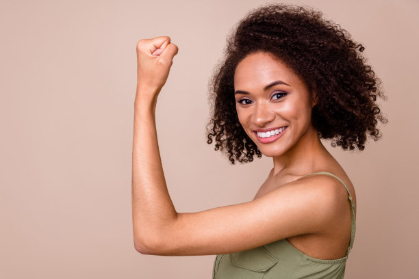 特写照片，展现了一位可爱、自信的年轻女性，波浪形的头发，展现女性力量，穿着时尚的卡其色服装，背景为米色。图片下载