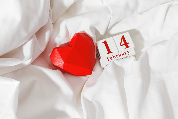 情人节概念，红色纸质心形情人卡和2月14日的假期日期放在床上白色皱褶的床单上，木制日历的俯视图，极简风格平铺照片，留白空间图片下载