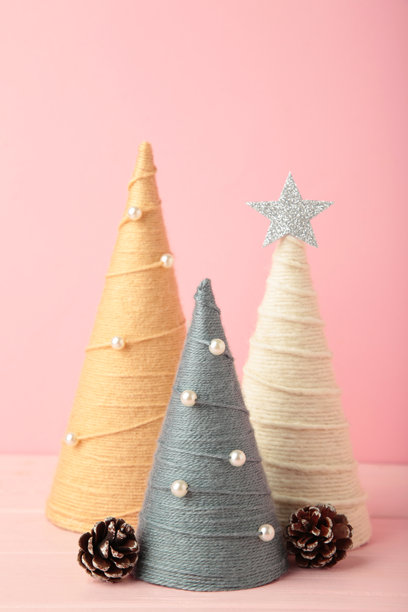 粉色背景上的手工圣诞树。用毛线包裹的锥形树。DIY概念。竖版照片图片下载