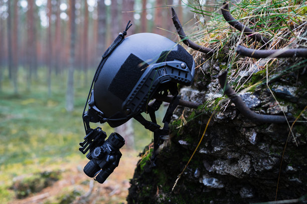安装在军用头盔上的夜视单筒望远镜，照片拍摄于靠近被摧毁的掩体的森林中。图片下载
