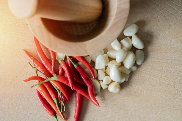从上方拍摄的小蒜和红辣椒的照片，背景是一个木质厨房桌子，上面有一个研钵和杵。图片下载