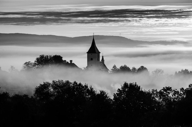 黑白教堂照片。宁静的日出映照在秋季乡村教堂的轮廓上，四周环绕着薄雾和闪耀的橙色天空。图片下载