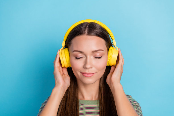 特写照片：年轻漂亮、梦幻可爱的女孩穿着条纹T恤，触摸新耳机，享受悦耳的音乐，背景为蓝色。图片下载
