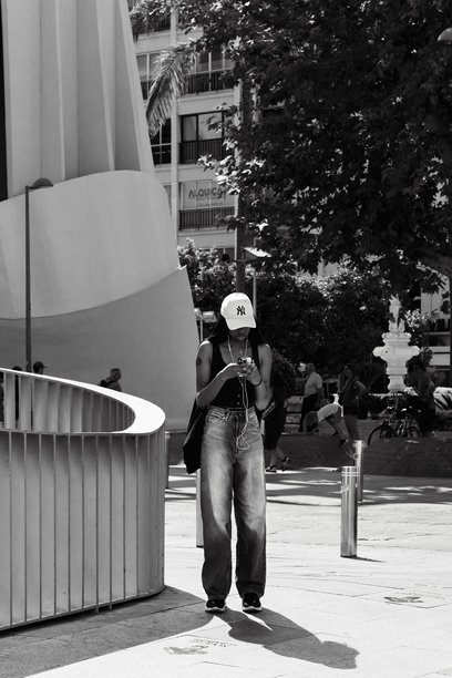 一张黑白照片，年轻女性穿着城市风格的服装，正在听音乐并用手机打字。图片下载