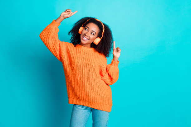 漂亮年轻女孩的照片肖像，耳机佩戴时尚针织服装，橙色服装，背景为水绿色，目光空洞。图片下载