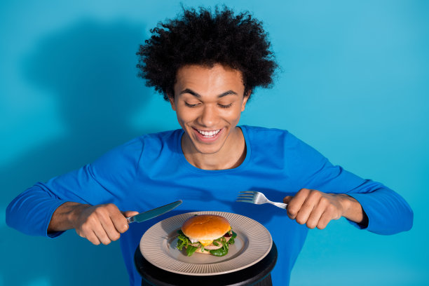 时尚年轻男子兴奋地吃汉堡的照片肖像，背景为蓝色。图片下载