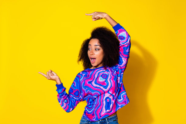 穿着时尚多彩蓝色衣服的迷人年轻女性在黄色背景下指向空旷的空间，拍摄的肖像照片。图片下载