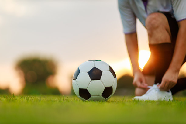 在黄昏日落下，足球场上，一名足球运动员正在户外运动，踢着足球，享受锻炼的乐趣，周围是一片绿色的草地。图片留有空白空间。图片下载