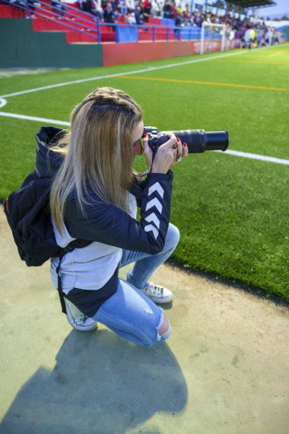 女性体育摄影师在黄昏比赛中蹲下拍摄足球场上的照片图片下载