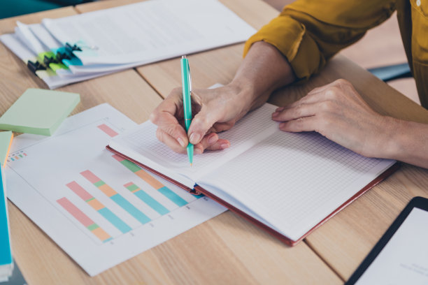 裁剪的照片，女士房地产经纪人穿着衬衫，微笑着在室内工作场所写报告。图片下载