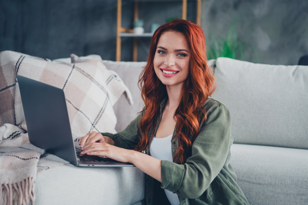 穿着卡其色衬衫的可爱女孩在室内公寓房间里使用现代电子设备打字的照片图片下载