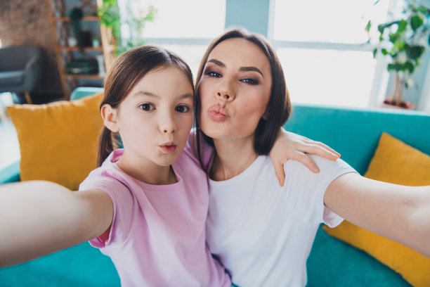 可爱的家庭照片，温馨的妈妈和女儿在室内客厅录制视频博客，享受假期周末。图片下载