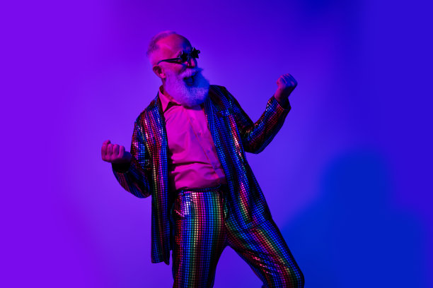 穿着五彩斑斓亮片条纹服装的酷炫老年男性舞者在蓝紫色霓虹灯背景下获胜的照片图片下载