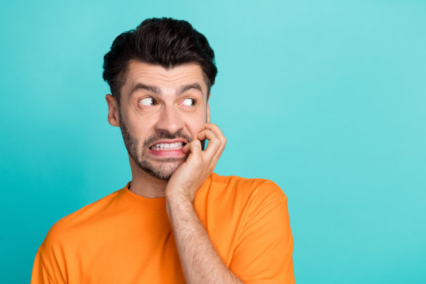 特写照片：年轻帅气、幽默迷人的男士穿着橙色T恤，咬着牙，神情紧张，目光空洞，背景为青色。图片下载