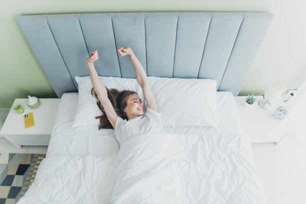 从上方拍摄的积极心态女性穿着睡衣在室内公寓的床上伸展身体的照片图片下载