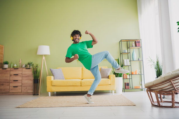 年轻男子在室内公寓的绿色环境中，举起拳头听音乐，享受周末时光的全身照片图片下载