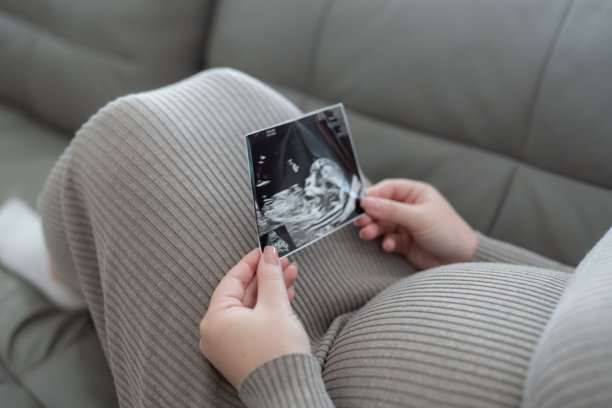 Z世代孕妇坐在沙发上，手中拿着胎儿的超声波扫描照片。孕期、产前护理的概念。图片下载