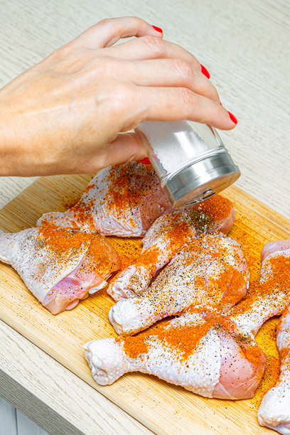 家庭主妇在厨房给生鸡腿撒盐，竖版照片图片下载