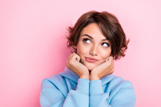 特写照片：年轻迷人女孩，梦幻般的好奇目光，轻触脸颊，迷人，背景为粉色，适合新促销。图片下载