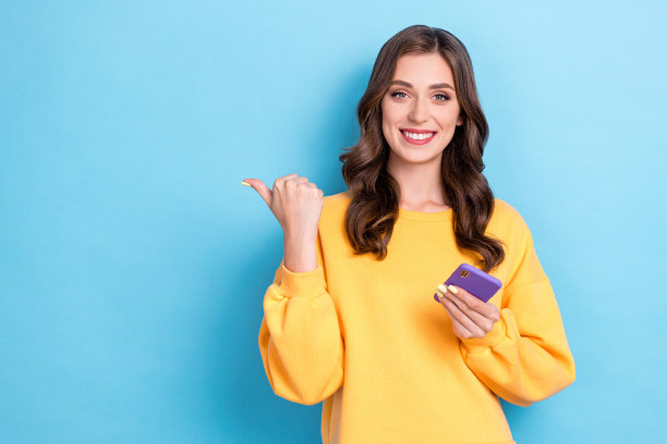 特写照片，年轻可爱迷人的女孩手持手机，手指指向空白处，推荐电子购物优惠，背景为蓝色。图片下载