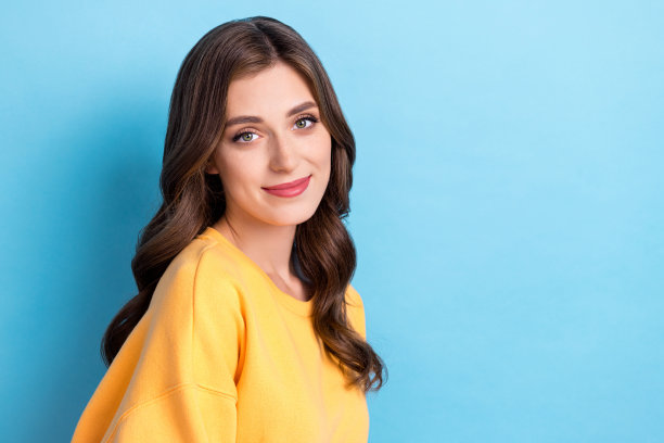 美丽年轻女性的照片肖像，美容院程序宣传海报，穿着时尚的黄色服装，背景为蓝色。图片下载