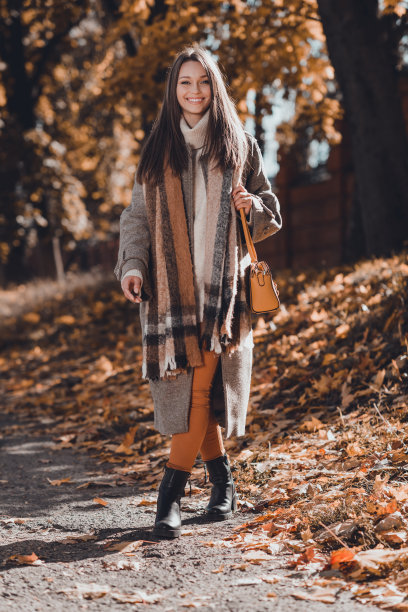 乐观的长发女士穿着外套、围巾、裤子和鞋子，在公园户外拍摄的竖版照片图片下载