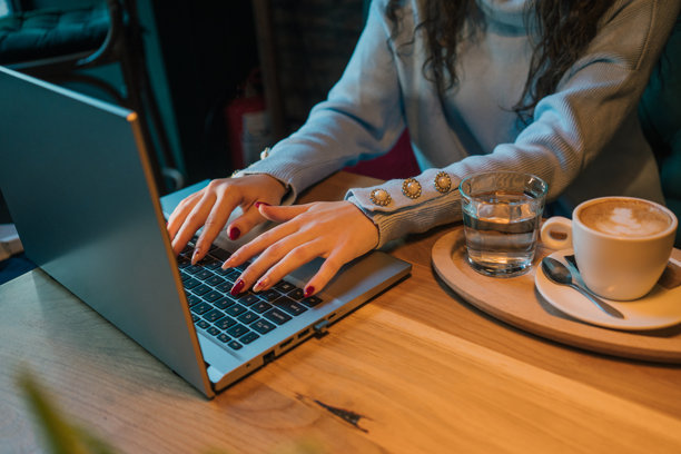 桌子上有一台笔记本电脑、一杯咖啡，以及熟练地在键盘上打字的双手，散发出专业和专注的气息。这张照片捕捉了现代企业环境的本质，散发出时尚的商业风格。图片下载
