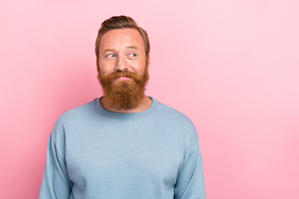 年轻迷人的红发胡子男士的肖像照片，面带积极满意的表情，背景为粉色，空旷的空间。图片下载