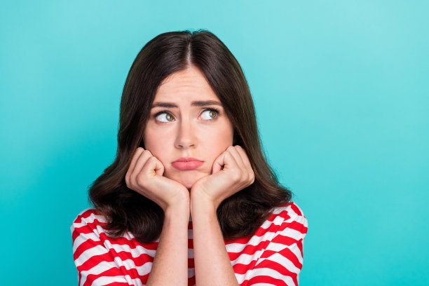 特写照片，年轻可爱的女孩穿着条纹T恤，手托下巴，表情不快，显得无聊，目光投向空旷的地方，背景为青色。图片下载