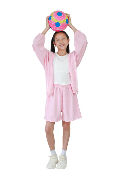 穿着粉色运动服的亚洲女孩站着，双手举着足球，背景为白色。全身照片。图片下载