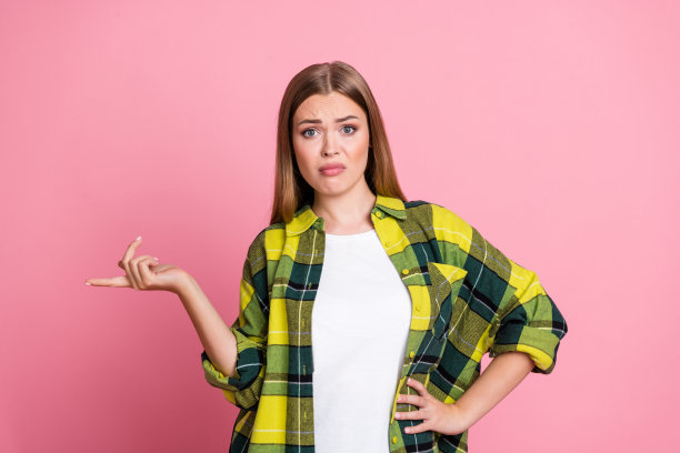 可爱的年轻女士的照片肖像，表现出恼怒和傲慢，指向空白处，穿着黄色格子衣服，背景为粉色。图片下载