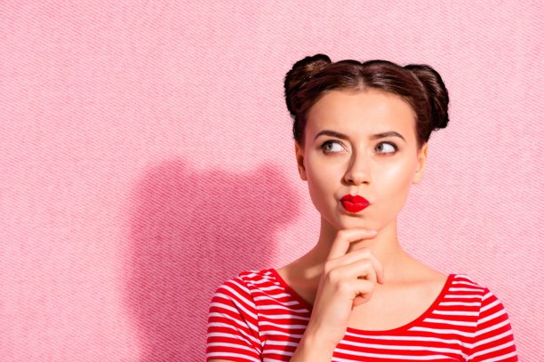 特写照片：美丽的女士，两个发髻，涂抹唇膏，手托下巴，仰望空旷的空间，沉思 contemplative，穿着休闲的红白条纹T恤，背景为粉色。图片下载