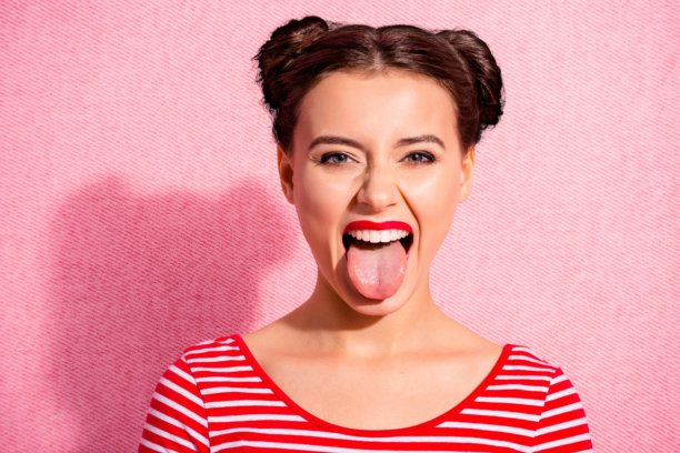 特写照片，漂亮的女士，粗心大意，俏丽的发型，两个发髻，明亮的发蜡，迷人的大嘴唇，吐出舌头，穿着休闲的红白条纹T恤，背景为粉色。图片下载