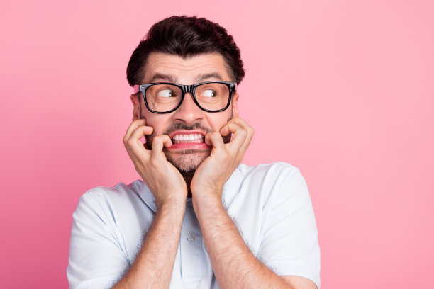 特写照片：年轻迷人的有胡子男士，穿着白色 polo 衫，紧张地咬着指甲，目光空洞，背景为粉色。图片下载