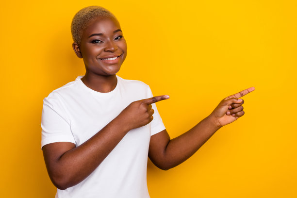 积极女孩的侧面照片，双手食指指向促销，穿着时尚衣服，背景为黄色，留有空白空间。图片下载